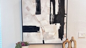 Una consola moderna con un cuadro abstracto grande, una planta en maceta y esculturas de madera.