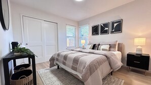 Un dormitorio con cama, mesitas de noche, una ventana y una puerta.