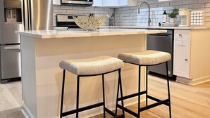Una cocina moderna con armarios blancos, electrodomésticos de acero inoxidable y una isla central con taburetes de bar.