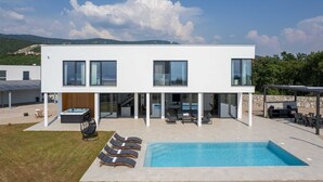 Una casa moderna de dos pisos con piscina, mobiliario de exterior y zona de barbacoa.