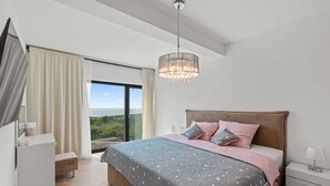 Un dormitorio con una cama grande, una mesita de noche, un aparador y vistas al exterior.