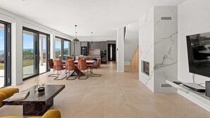 Una sala de estar moderna con un televisor grande, un comedor con mesa y sillas, y una cocina al fondo.