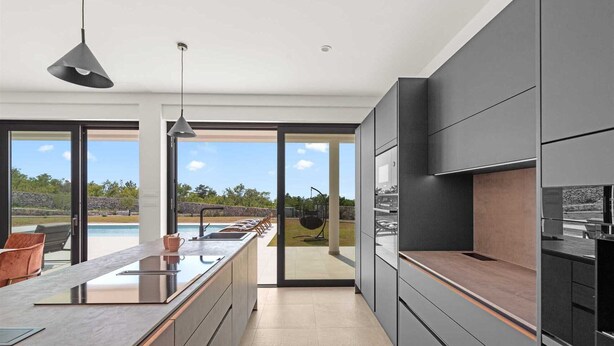Una cocina moderna con una isla grande, muebles oscuros y vistas a una piscina.