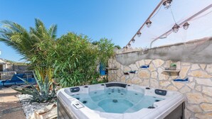Un jacuzzi en un jardín con muros de piedra y un cielo azul despejado.