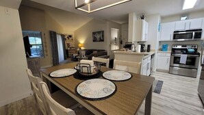 A modern kitchen with white cabinets, stainless steel appliances, and a dining area with a wooden table and chairs.
