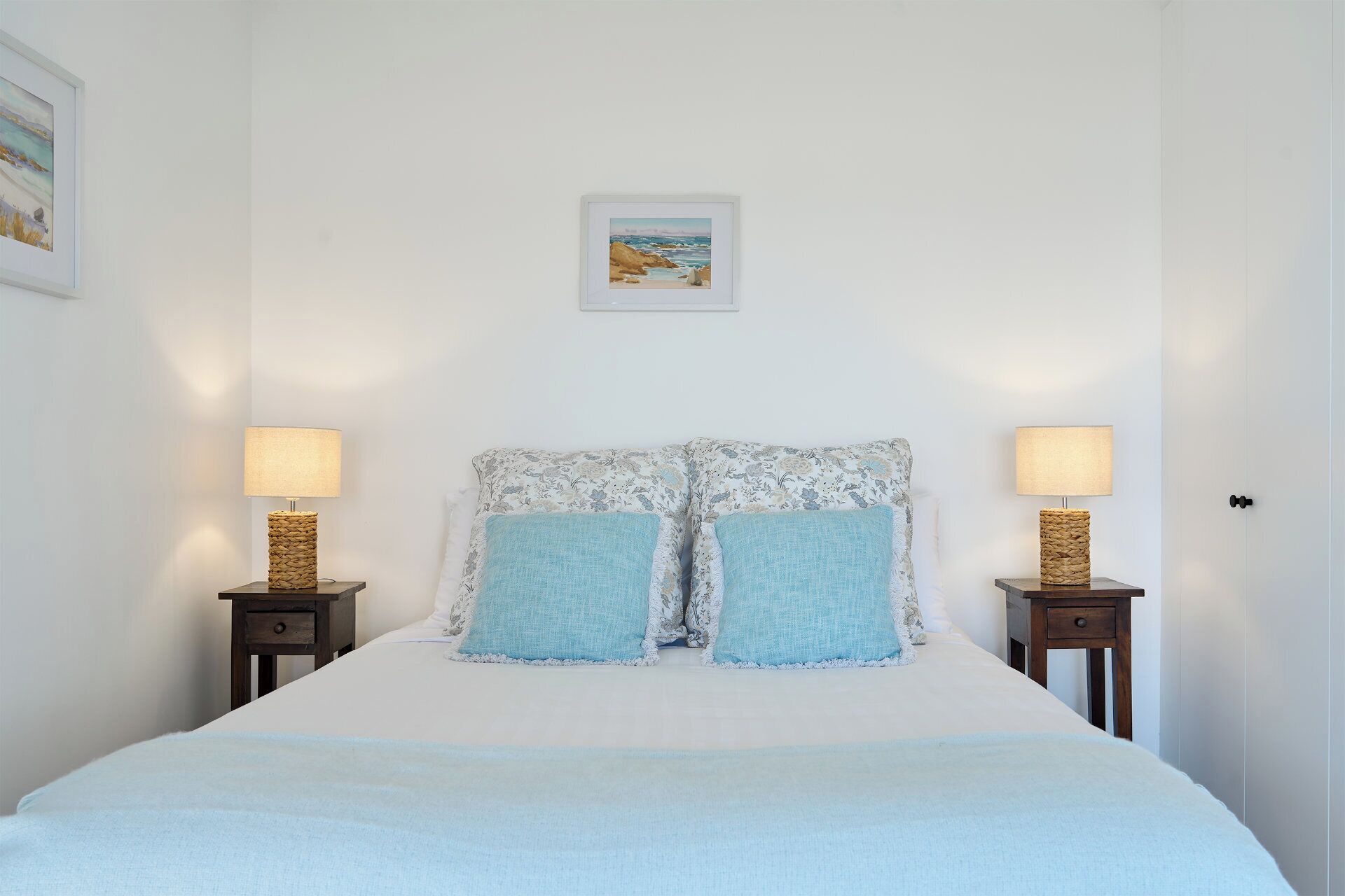 Un dormitorio con una cama, dos mesitas de noche, dos lámparas y un cuadro en la pared.