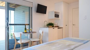 A modern bedroom with a bed, a small table with chairs, a TV mounted on the wall, and a kitchenette area. - Bicheno Ocean Views Apt 2 - Bicheno Accommodation (Bicheno)