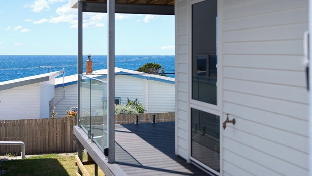 A coastal house with a balcony overlooking the sea, a wooden deck, and a fenced backyard. - Bicheno Ocean Views Apt 2 - Bicheno Accommodation (Bicheno)