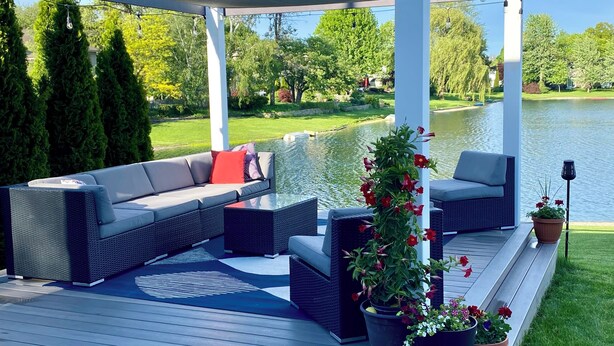 Un espace extérieur aménagé, abrité et doté de sièges, avec vue sur la piscine, comprenant un canapé, des fauteuils et des plantes en pot.