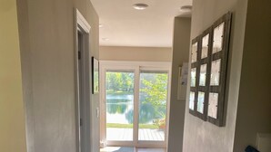 Un couloir au plancher de bois menant à une porte vitrée donnant sur un jardin et un étang.