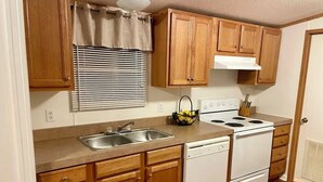Cocina compacta con armarios de madera, estufa blanca, pileta y lavavajillas.