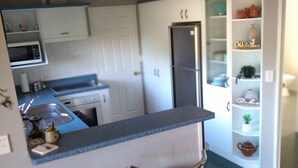 A compact kitchen with a bar area, two stools, and a refrigerator. - Cherry Tree Lane Accommodation, Quiet location bordered by farmland. (Te Awamutu)
