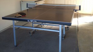 A ping pong table with wheels in a room with white walls and a door in the background. - Cherry Tree Lane Accommodation, Quiet location bordered by farmland. (Te Awamutu)