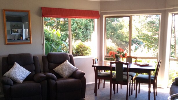 A living room with a sofa, a dining table with chairs, and a kitchen area with a counter. - Cherry Tree Lane Accommodation, Quiet location bordered by farmland. (Te Awamutu)