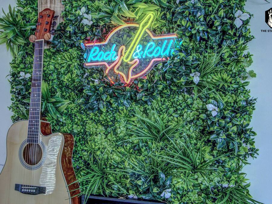 A guitar leaning against a wall with a neon sign that reads 'Rock & Roll'.