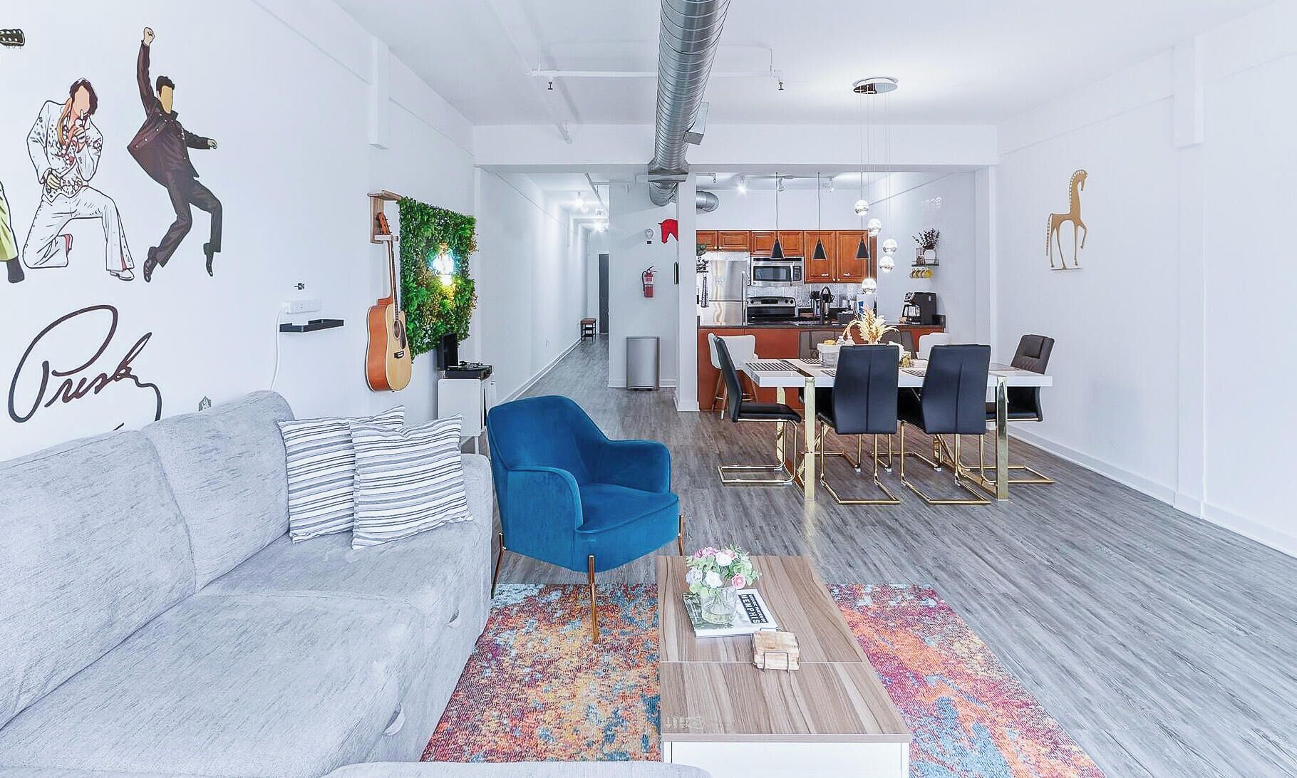 A modern living room with a grey sofa, a blue armchair, and a dining area with a table and chairs.