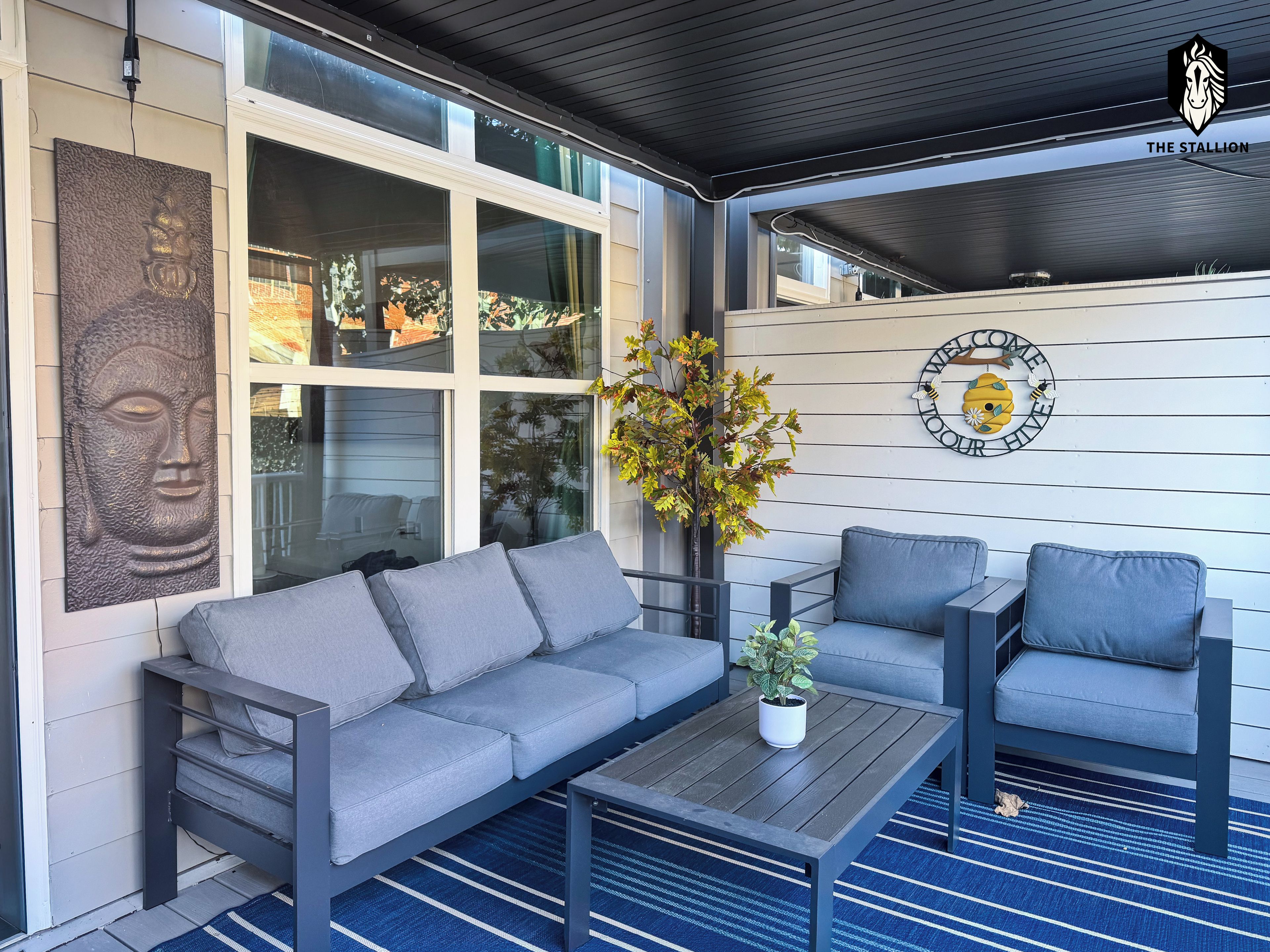 A modern outdoor seating area with a sofa and chairs, a coffee table, and a decorative wall with a Buddha relief and a welcome sign.