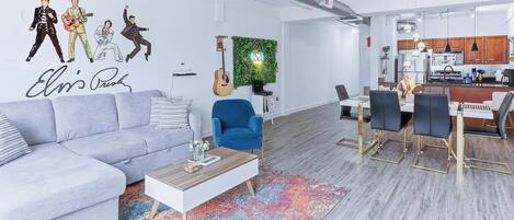 Un salón moderno con un sofá gris, un sillón azul y un comedor con una mesa blanca y sillas negras.