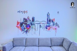 A colorful cityscape wall art with the word "Memphis" above it, placed above a grey sofa.