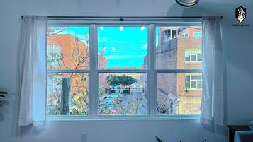 A room with a large window offering a view of a cityscape, including buildings and a tree.
