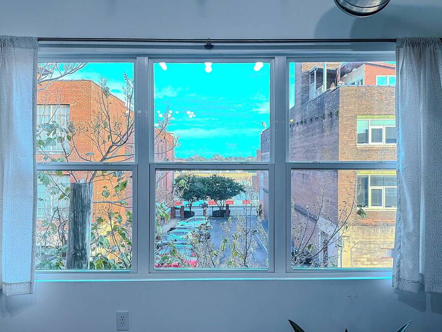 A room with a large window offering a view of a cityscape, including buildings and a tree.
