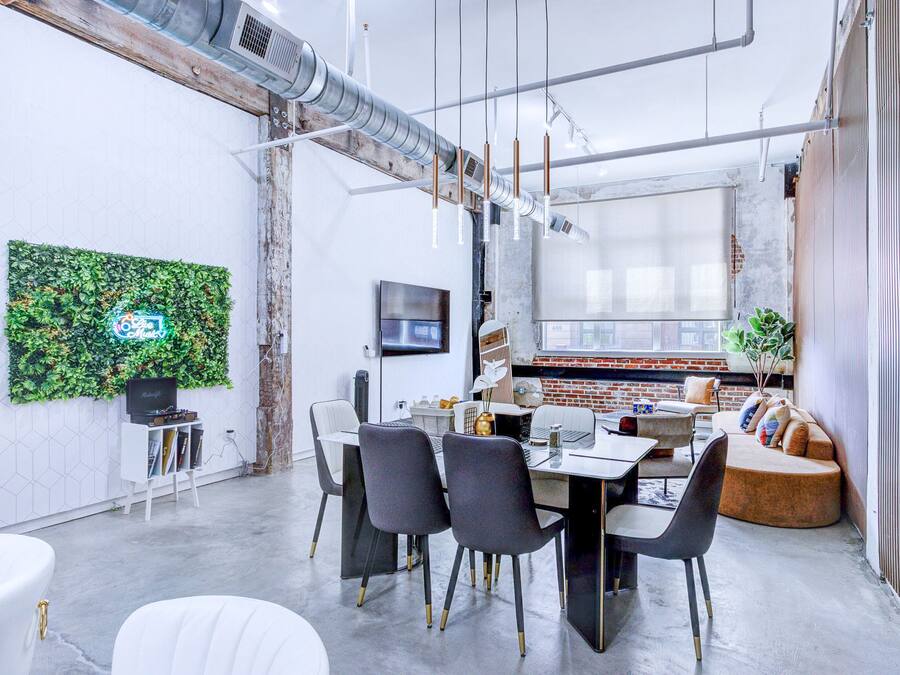 A modern office space with a dining area, a large green wall, and a brick wall with a window.