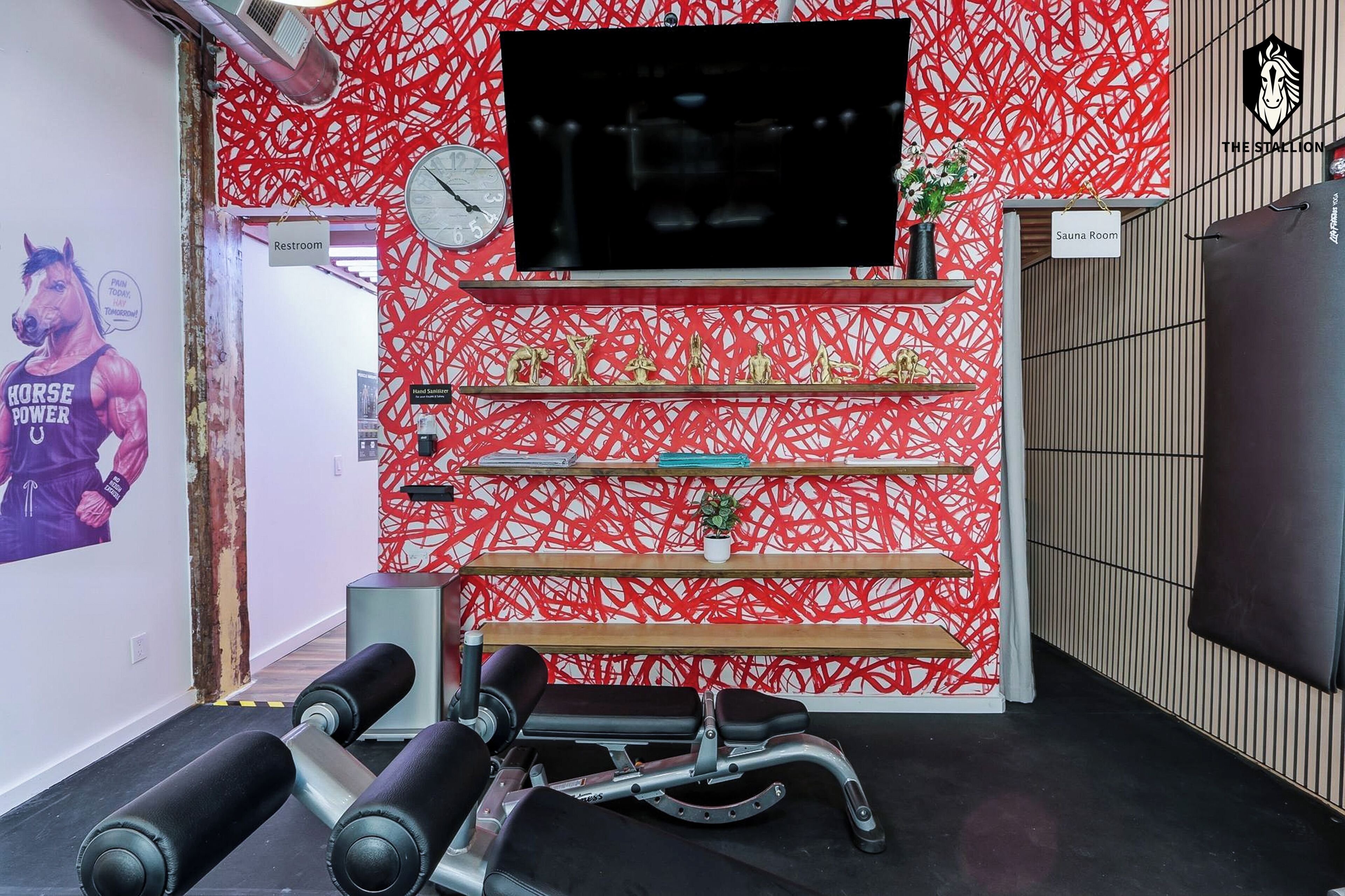 A gym with a red patterned wall, a mounted TV, and exercise equipment.