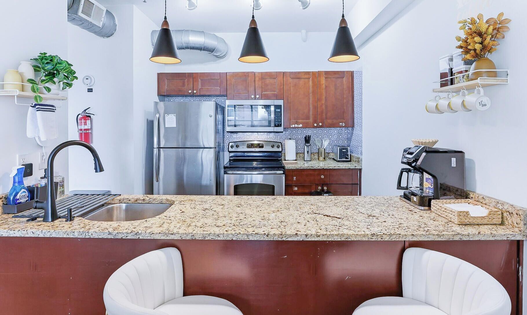 Cocina moderna con electrodomésticos de acero inoxidable, encimera de granito e iluminación colgante.