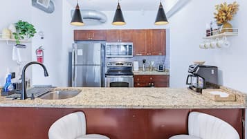 Cocina moderna con electrodomésticos de acero inoxidable, encimera de granito e iluminación colgante.