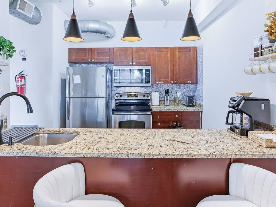 Cocina moderna con electrodomésticos de acero inoxidable, encimera de granito e iluminación colgante.