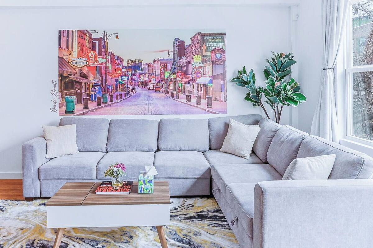 A living room with a gray sofa, a coffee table, and a large cityscape painting on the wall.
