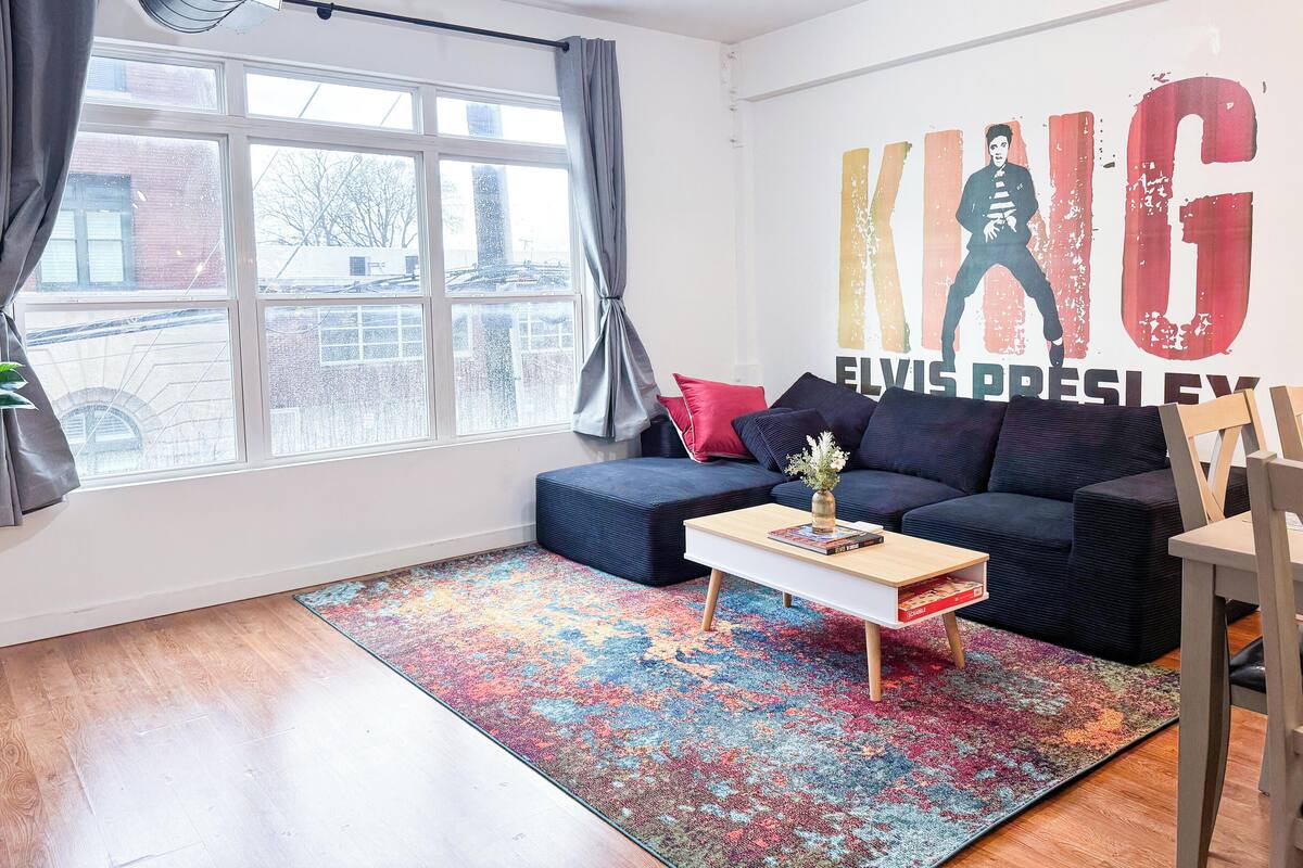 A modern living room with a large window, a blue sofa, a colorful rug, and a wall with a poster.