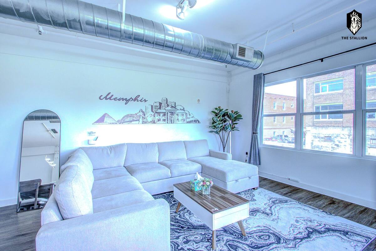 A modern living room with a white sofa, a coffee table, and a cityscape mural on the wall.