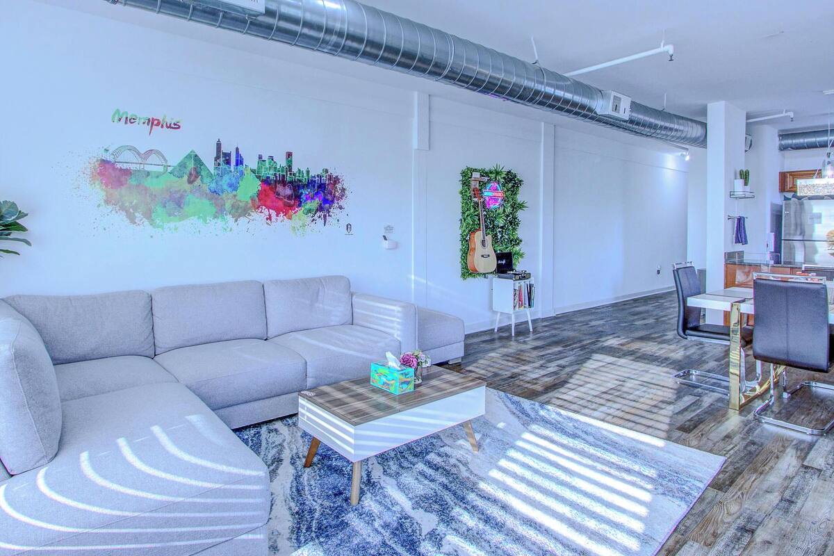 A modern living room with a gray sofa, a wooden coffee table, and a colorful wall mural.