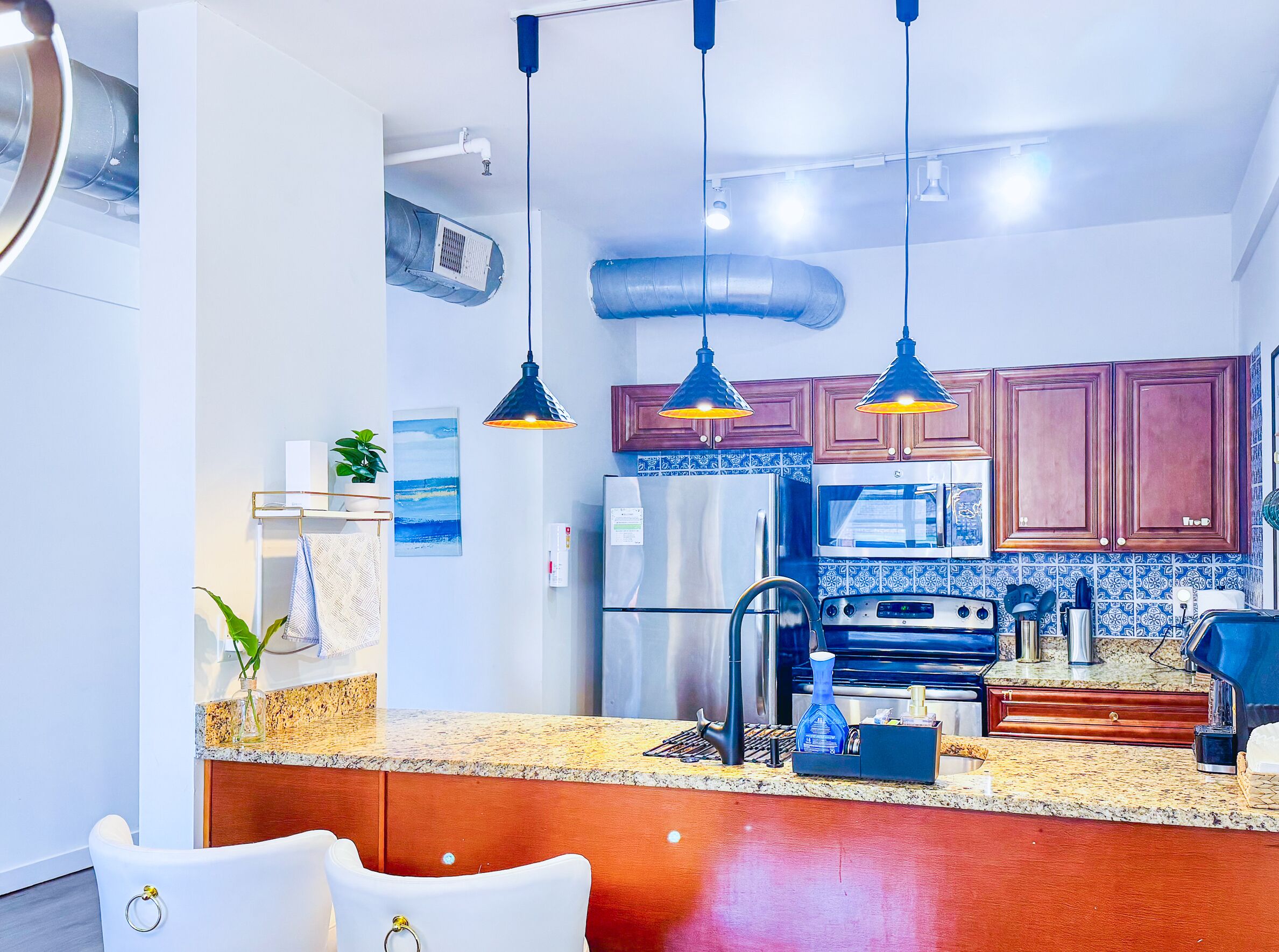 A modern kitchen with granite countertops, stainless steel appliances, and pendant lighting.