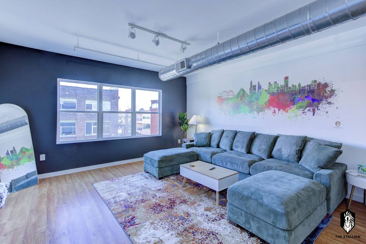 A modern living room with a sectional sofa, a coffee table, and a colorful abstract painting on the wall.