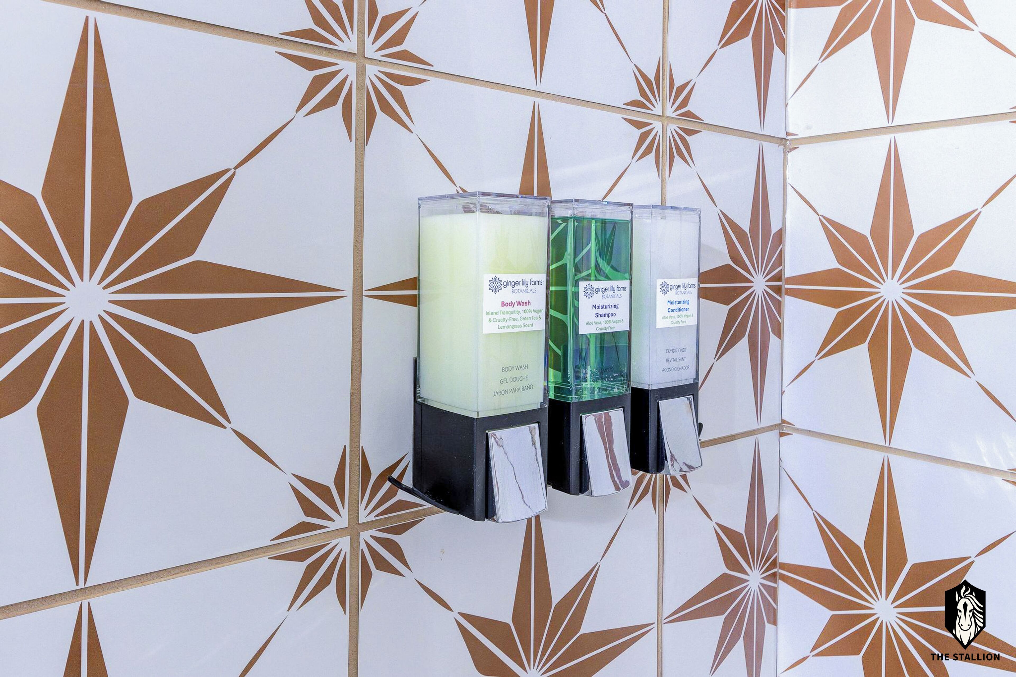 A wall-mounted dispenser with three bottles labeled for body wash, moisturizing shampoo, and conditioning cream.