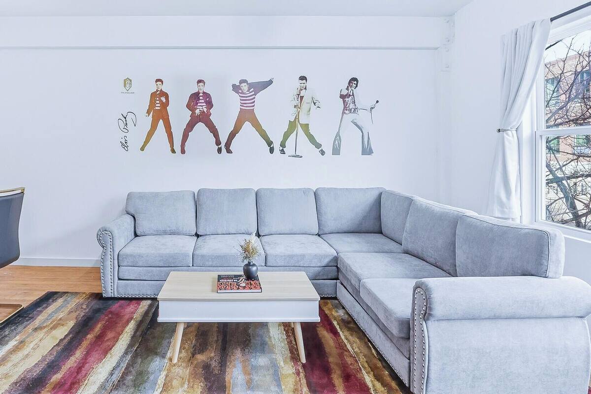 A modern living room with a grey sectional sofa, a coffee table, and a colorful striped rug.