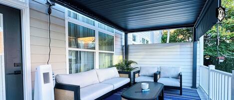 A covered outdoor seating area with a sofa, two chairs, a coffee table, and a floor heater.
