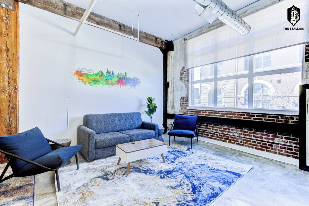 A modern living room with a sofa, armchairs, a coffee table, and a large window with a cityscape view.