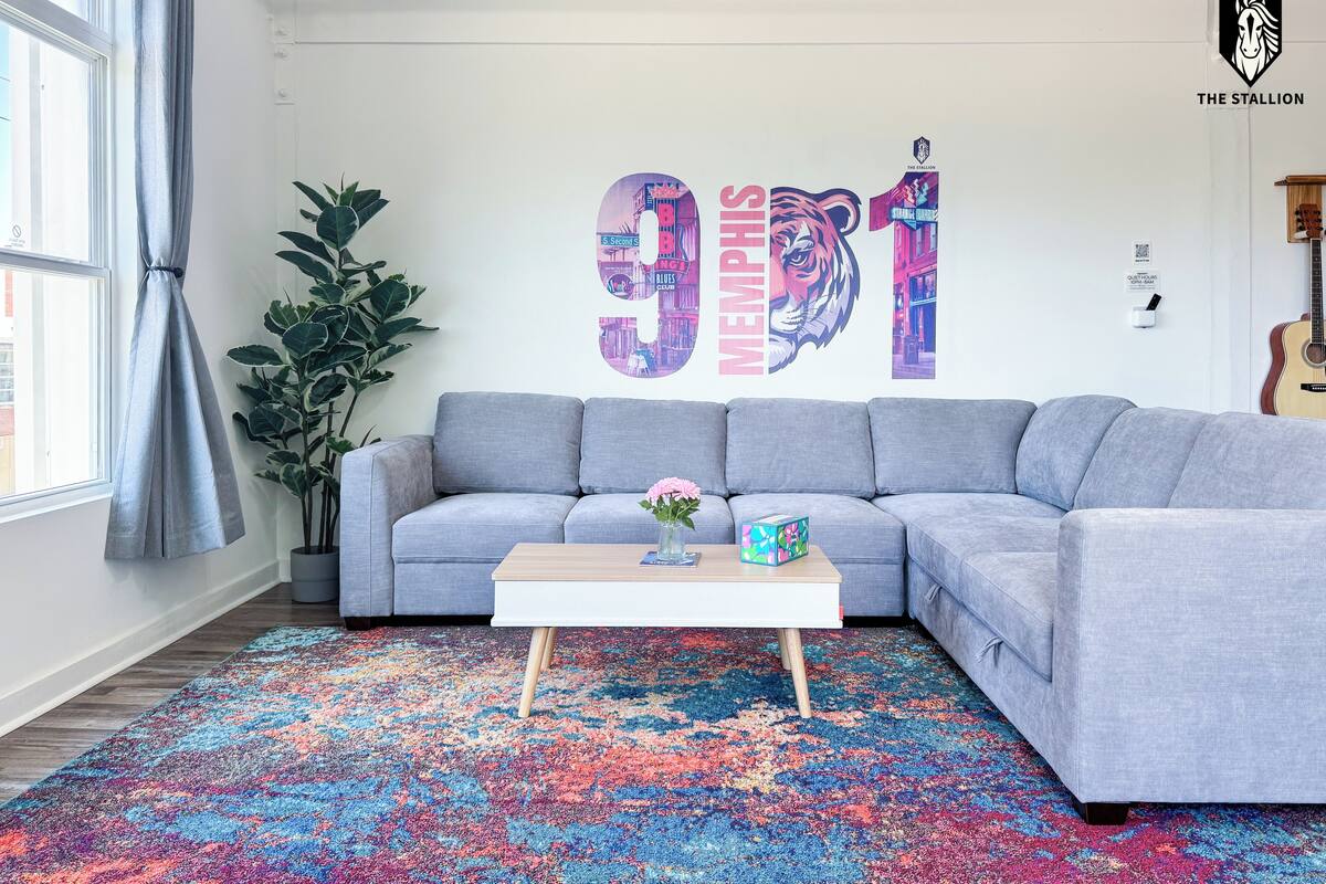 A modern living room with a grey sofa, a colorful rug, and a wall with a large graphic.