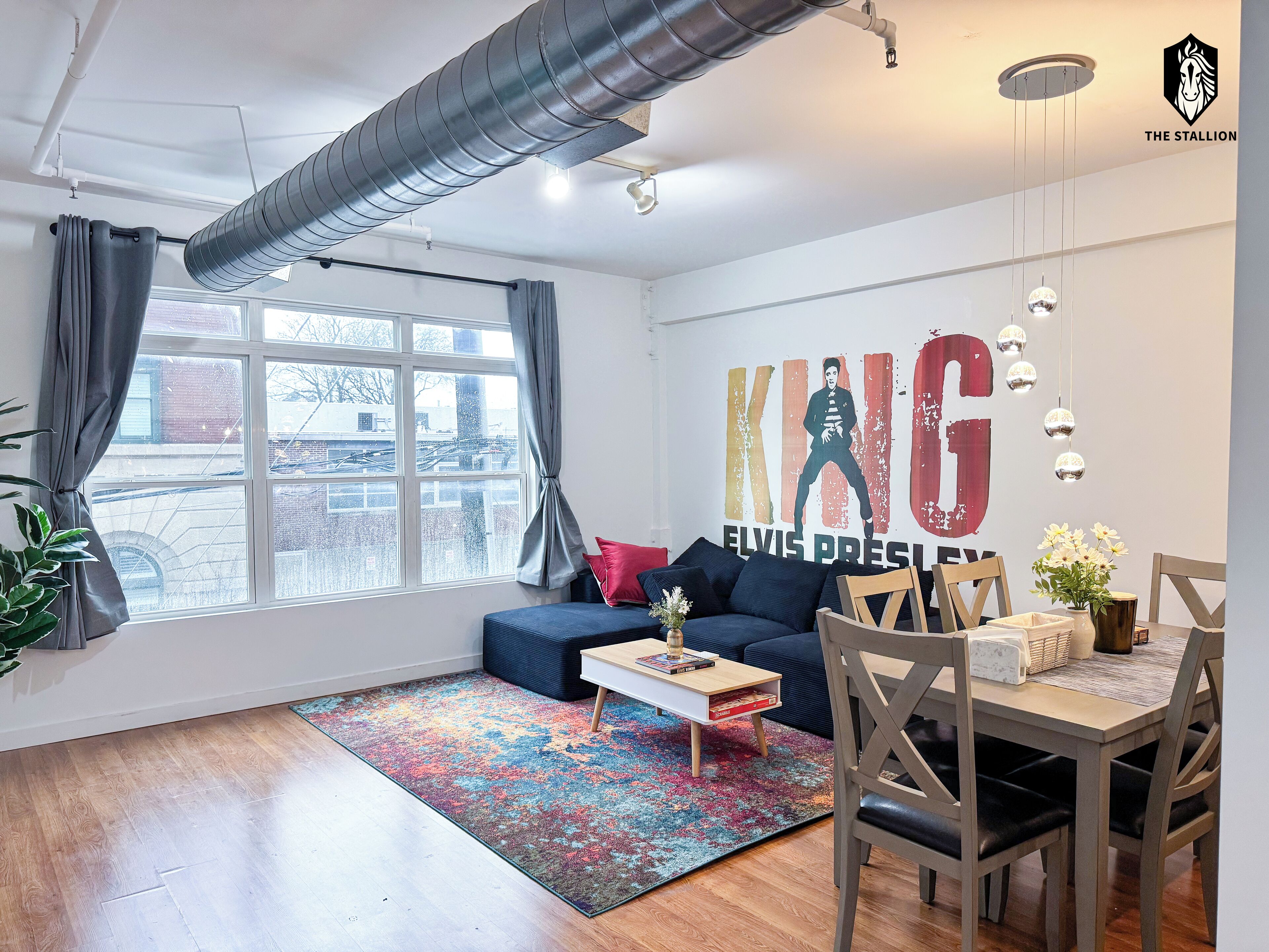 Ein modernes Wohnzimmer mit großem Fenster, einem blauen Sofa, einem Holztisch und einem Essbereich mit Tisch und Stühlen.