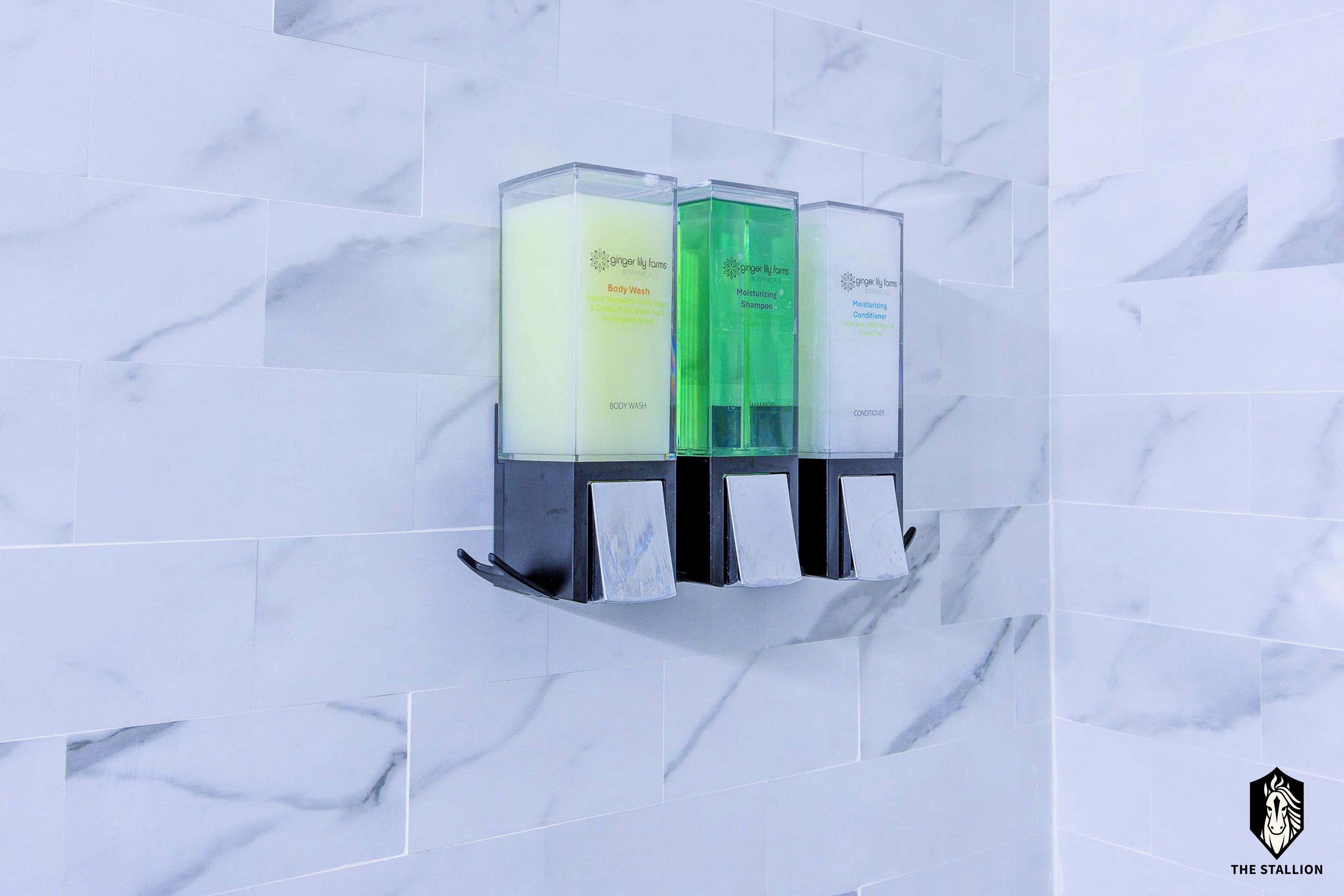 A wall-mounted dispenser with three bottles labeled "Body Wash," "Moisturizing Shampoo," and "Conditioner."