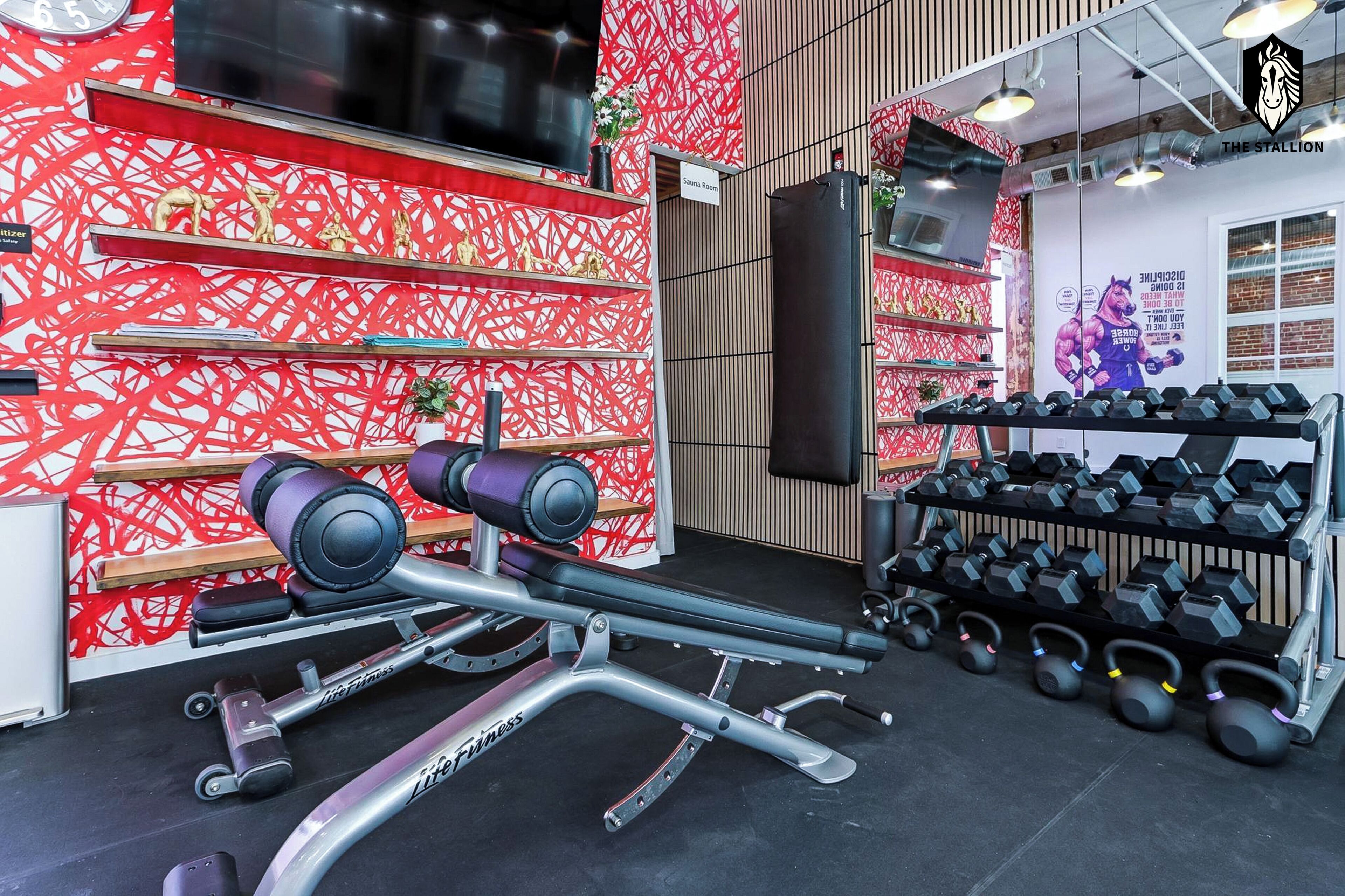 A gym with weightlifting equipment, dumbbells, and a sauna room.