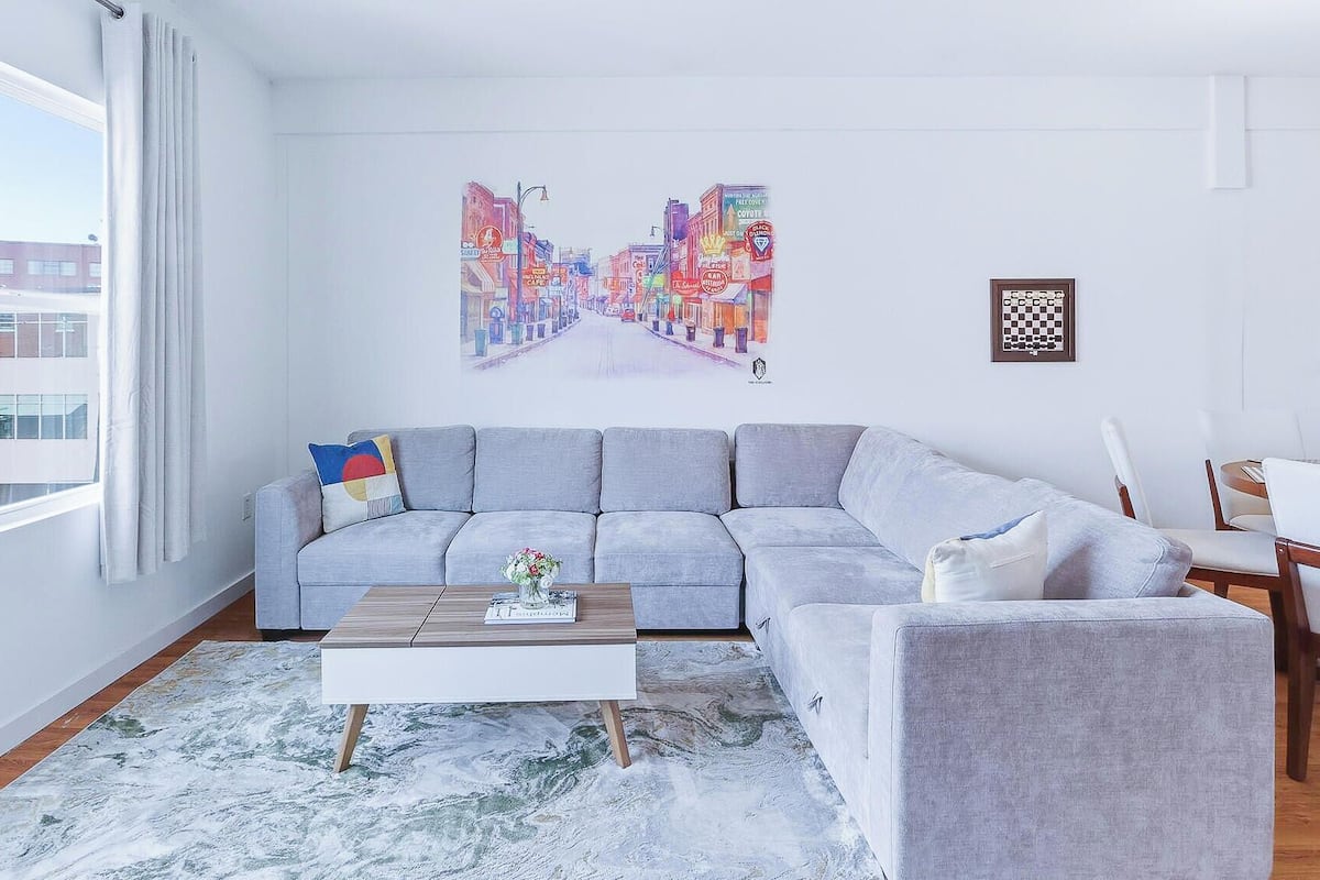A living room with a gray sectional sofa, a coffee table, and a cityscape painting on the wall.