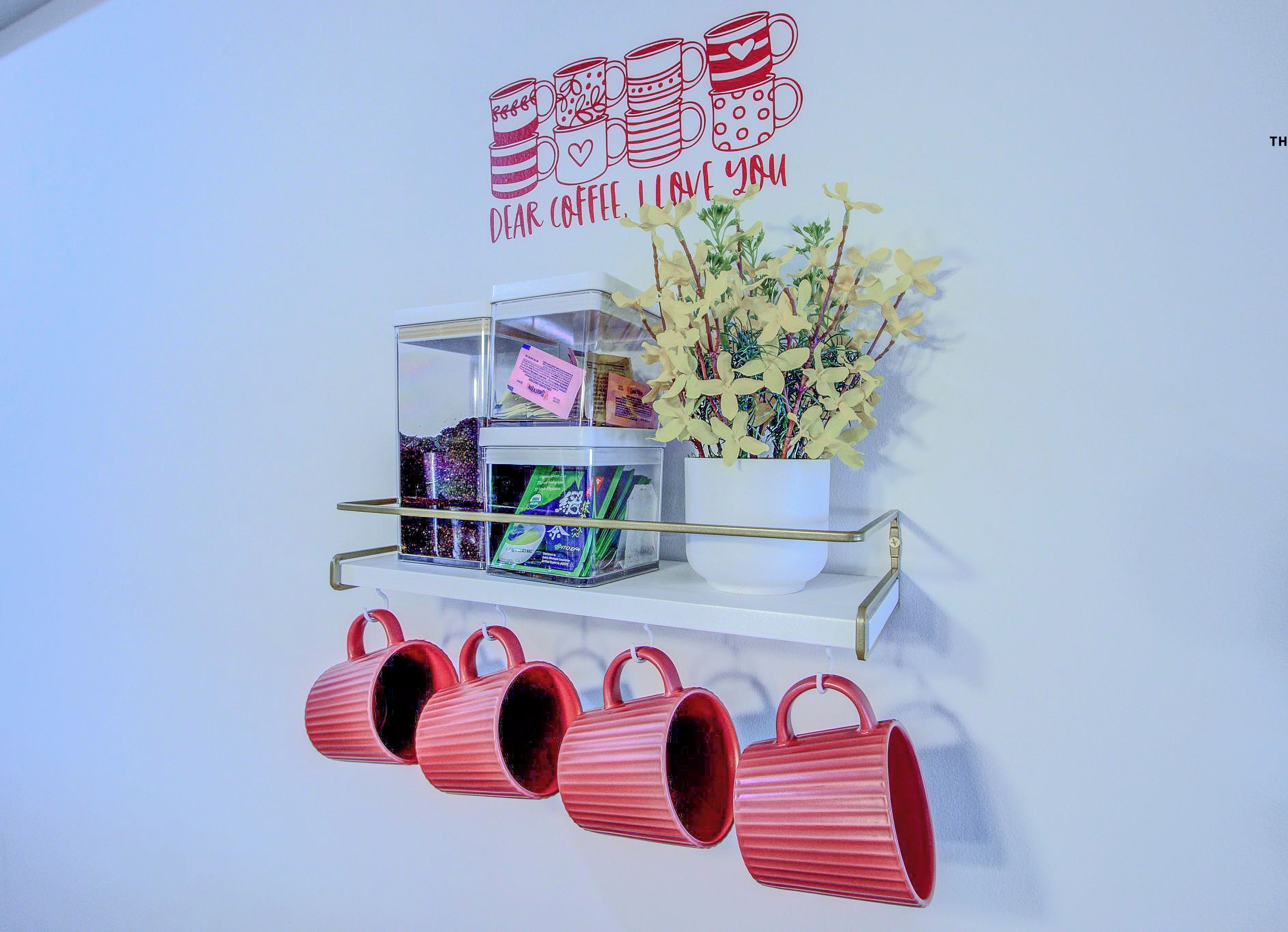 A wall with a coffee-themed decoration, a shelf with coffee products, and a potted plant.