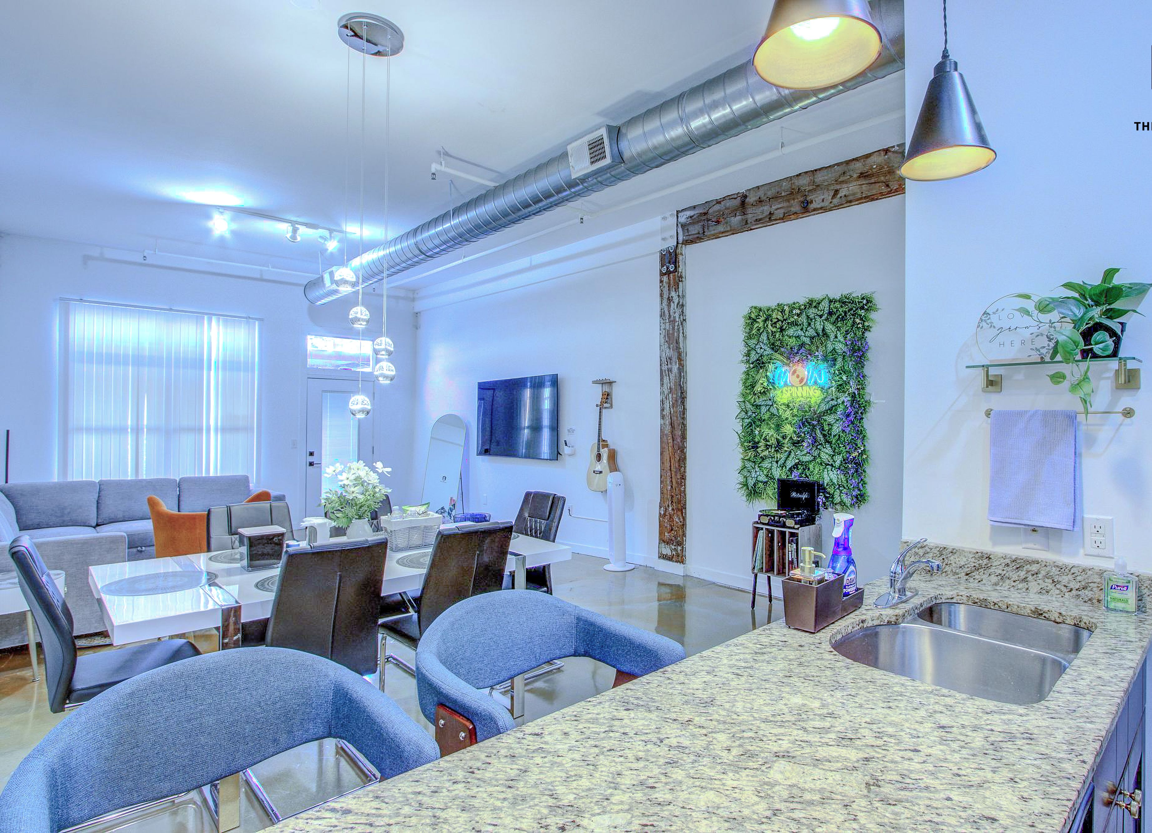 A modern kitchen with granite countertops, a stainless steel sink, and a dining area with a glass table and chairs.