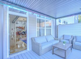 A covered outdoor area with wicker furniture, a wooden table, and a sliding glass door leading to an interior space.