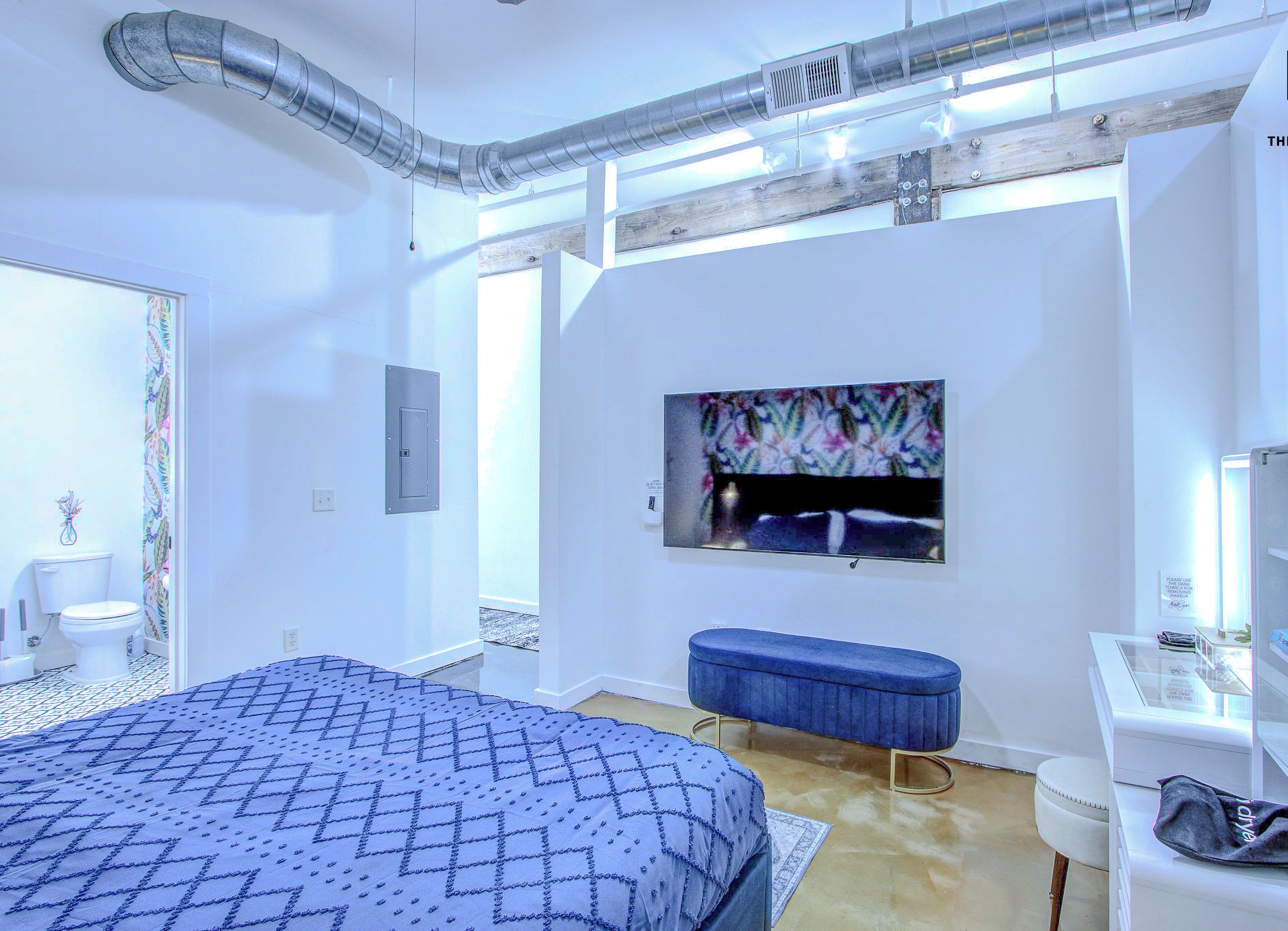 A modern bedroom with a large bed, a bench, a TV, and a desk with a mirror.