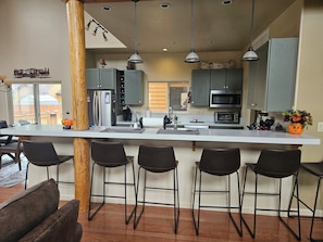 A modern kitchen with a central island, bar stools, and a view of the outdoors.